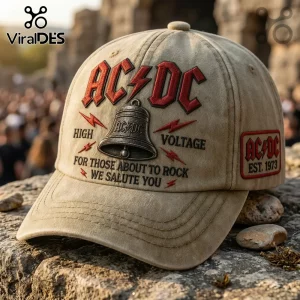 Distressed tan AC/DC baseball cap, red logo, bell graphic, black text 'HIGH VOLTAGE FOR THOSE ABOUT TO ROCK WE SALUTE YOU' 'EST. 1973'!