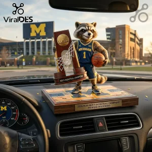 Raccoon figure in Michigan Wolverines jersey holding NCAA championship trophy on car dashboard with school stadium background!