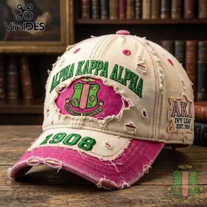 Distressed cream and pink baseball cap with green Alpha Kappa Alpha embroidery and 1908 text on a wooden table!