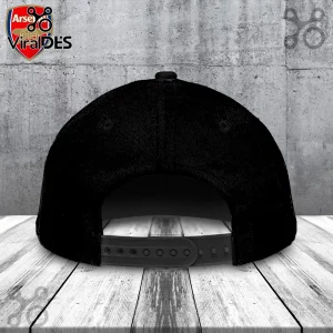 Back view of a plain black baseball snapback cap on a wooden surface against a grey concrete wall background!