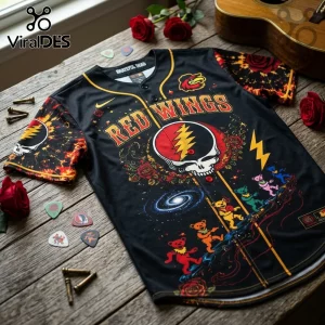 Black baseball jersey featuring Grateful Dead Red Wings graphic, dancing bears, roses, and lightning bolt on wood table.!