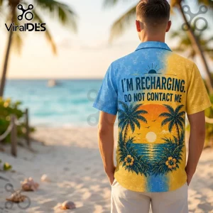 Man wearing a blue and yellow tropical button-down shirt with text reading I'M RECHARGING. DO NOT CONTACT ME at a beach.!