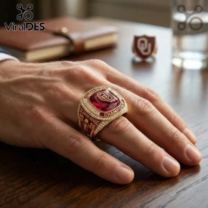 Gold Oklahoma Sooners championship ring with a large red center stone and white crystals on a person's hand.!