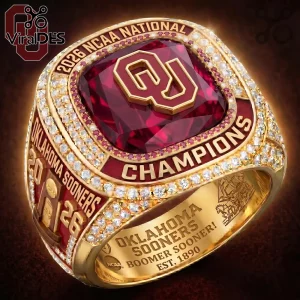 Oklahoma Sooners 2026 NCAA championship ring featuring a red gemstone, gold finish, and etched text on a brown background.!