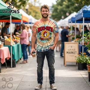 Man wearing a tie-dye t-shirt with a Buc-ee's beaver logo, tropical palm trees, and text reading EST. 1982 at a market.!