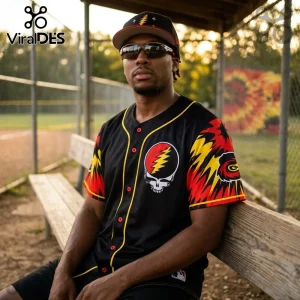Man wearing a black Grateful Dead baseball jersey with red and yellow lightning bolt emblem sitting on a wooden bench.!