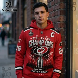Man wearing red Carolina Hurricanes Stanley Cup Champions hoodie with trophy graphic and 2026 text against brick wall.!