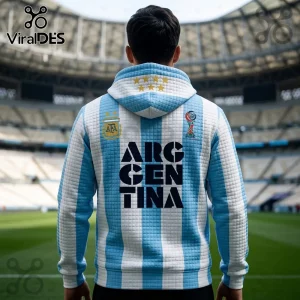 Man wearing a light blue and white striped Argentina hoodie with text ARGENTINA, AFA logo, and six gold stars at stadium.!