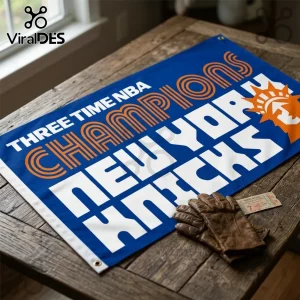 Blue New York Knicks banner featuring orange and white text reading Three Time NBA Champions on a wood table with gloves.!