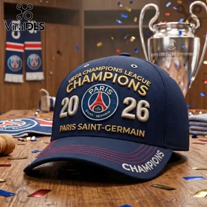 Navy blue PSG baseball cap with gold Champions 2026 embroidery, club crest, and red stitching on a wooden locker room table.!