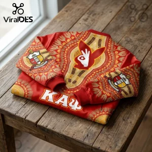 Kappa Alpha Psi crimson bomber jacket with gold African-inspired patterns, fraternity crests, and text on a wood surface.!