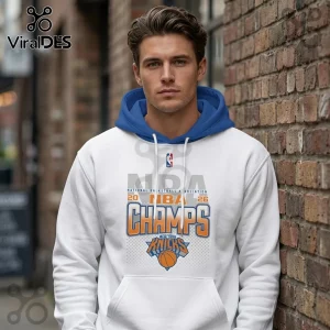 Man wearing a white hoodie with blue hood and 2026 New York Knicks NBA Champions graphic standing by a brick wall.!