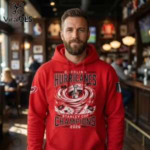 Man wearing a red Carolina Hurricanes Stanley Cup Champions 2026 hoodie with a graphic of a storm and the Stanley Cup trophy.!