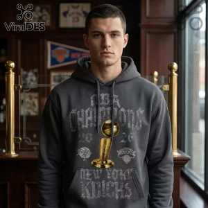 Man wearing a charcoal gray hoodie featuring NBA Champions 2026 New York Knicks text and a gold Larry O'Brien trophy graphic.!