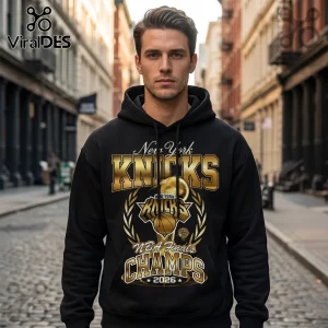 Man wearing a black pullover hoodie with gold New York Knicks 2026 NBA Finals Champs graphic on a cobblestone city street.!