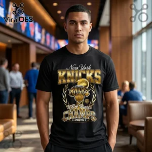 Man wearing a black t-shirt with gold New York Knicks 2026 NBA Finals Champions graphic in a blurred sports bar setting.!