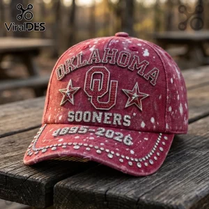 Red distressed denim cap with rhinestones, Oklahoma Sooners logo, stars, and 1895-2026 text on a wooden picnic table.!