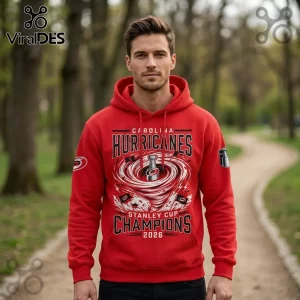 Man wearing red Carolina Hurricanes Stanley Cup Champions 2026 hoodie with black and white cyclone graphic in a park.!
