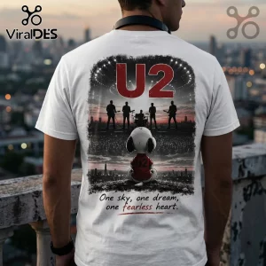 White t-shirt showing Snoopy watching a U2 concert silhouette on a city stage, with the text One sky, one dream, one fearless heart.!