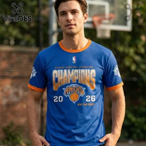 Man wearing a blue and orange New York Knicks 2026 Champions t-shirt with NBA logo on a basketball court background.!