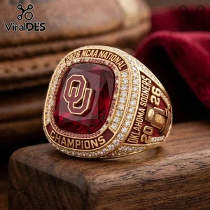 2026 NCAA Oklahoma Sooners championship ring with large red stone, gold finish, and diamond accents on wooden base.!