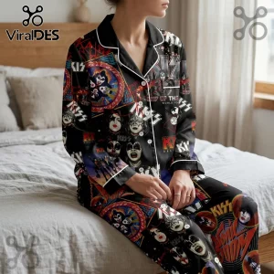 Woman wearing black satin pajamas featuring a vintage KISS band collage print with white piping on a bed.!