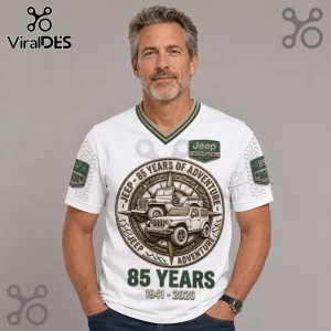 Man wearing a white V-neck Jeep 85th anniversary t-shirt with a compass graphic, off-road vehicle icons, and green patches.!