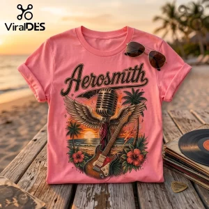 Pink Aerosmith t-shirt with tropical sunset graphic, microphone, wings, and electric guitar design on wooden beach deck.!