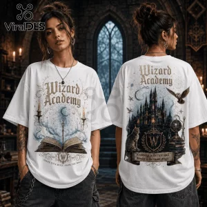 White oversized t-shirt featuring Wizard Academy text, open spellbook, castle, owl, and cat graphics in vintage style.!