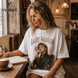 Woman wearing white oversized t-shirt with vintage Barry Manilow graphic, microphone, candles, and text at a cafe table.!