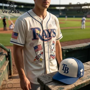 Cream baseball jersey with Rays logo, Snoopy, rockets, and US flags, plus a matching TB logo cap on a wooden dugout bench.!