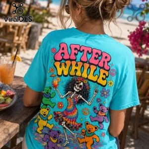 Turquoise t-shirt featuring a dancing skeleton in a tie-dye dress surrounded by colorful cartoon bears and flower art.!