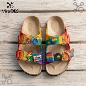 Rainbow ombre slide sandals with cork footbeds, metal buckles, and diverse decorative charms on a light wood surface.!
