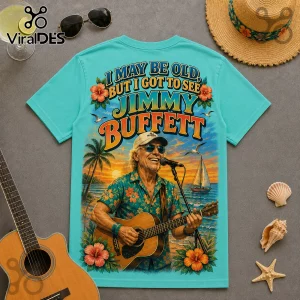 Jimmy Buffett I May Be Old Turquoise T-Shirt featuring a graphic of the singer playing guitar on a tropical beach.