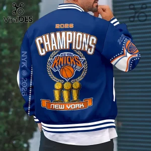 Blue New York Knicks 2026 Champions varsity jacket with basketball trophy graphic and white and orange lettering.!
