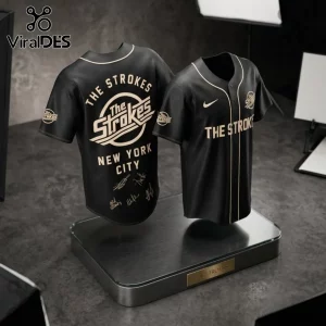 The Strokes Reality Awaits 2026 Tour black baseball jersey featuring band logo, NYC text, and signatures on display stand.