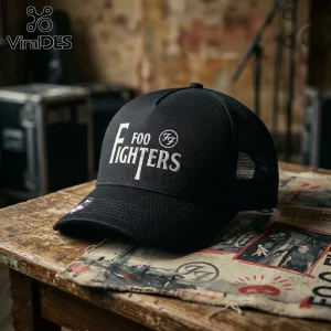 Black trucker hat with white embroidered Foo Fighters logo resting on a rustic wooden table with vintage paper scraps.!