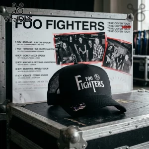 Black trucker hat with white embroidered Foo Fighters logo resting on a music equipment case in front of a tour poster.!