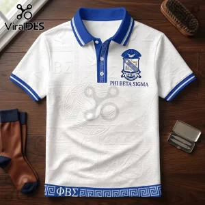 Phi Beta Sigma white polo shirt with blue trim, Greek letter patterns, and a dove emblem on a dark wooden surface.!