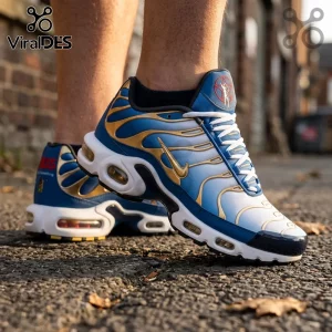 Nike Air Max Plus sneakers in blue, white, and gold with a pentagram logo on the tongue, worn on a brick-paved surface.!