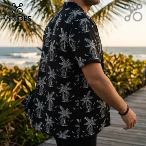Man wearing a black short-sleeve shirt with white palm tree and hula dancer patterns at a beach boardwalk.!