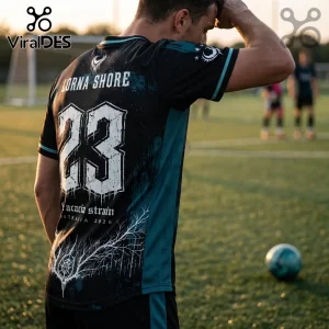Man wearing black Lorna Shore sports jersey with number 23, Acacia Strain text, and white tree graphics on a grass field.!