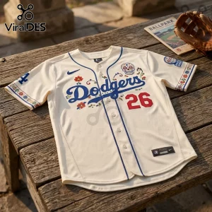 Los Angeles Dodgers Dia De Los Muertos cream baseball jersey with floral embroidery and number 26 on a wooden bench.