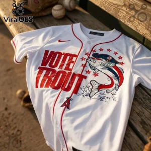 White baseball jersey with red text reading VOTE TROUT, a fish wearing a pirate hat, and red stars on a wooden bench.!