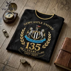 Newcastle United black t-shirt featuring a 135 years anniversary graphic, gold text, and team crest on wooden background.!