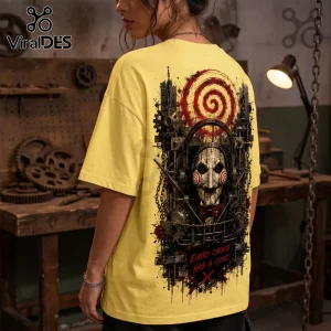 Yellow t-shirt featuring Saw Jigsaw puppet graphic with industrial gears, red spiral, and text Every Choice Has A Cost.!