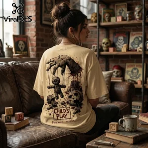 Woman wearing cream t-shirt with Chucky horror movie print featuring voodoo doll, bloody hand, blocks, and Chucky text.!
