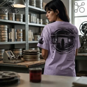 Woman wearing a lavender cotton t-shirt with a black horror movie graphic depicting a girl and VHS tape on the back.!