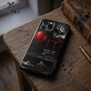 iPhone case featuring Pennywise the clown, a red balloon, and the quote Every fear floats to the surface on a wooden desk.!