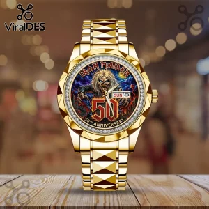 Gold-tone metal watch with Iron Maiden Eddie mascot graphic, rhinestone bezel, and 50th anniversary dial on wood table.!